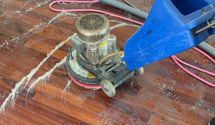 A floor cleaning machine is operating on a wooden floor