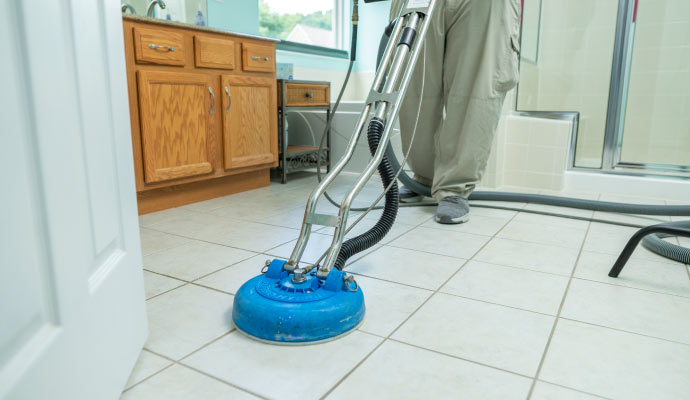 Person cleaning tile floor with cleaning machine